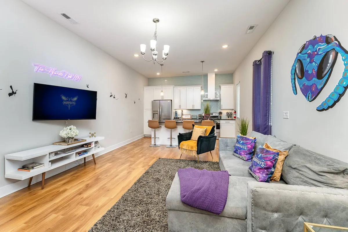 The hero image showcases a lively, open-concept living area with a plush sofa accented by vibrant cushions, eye-catching neon wall art adding a fun urban vibe, and a modern dining space with sleek bar stools—all designed for relaxation and entertaining.