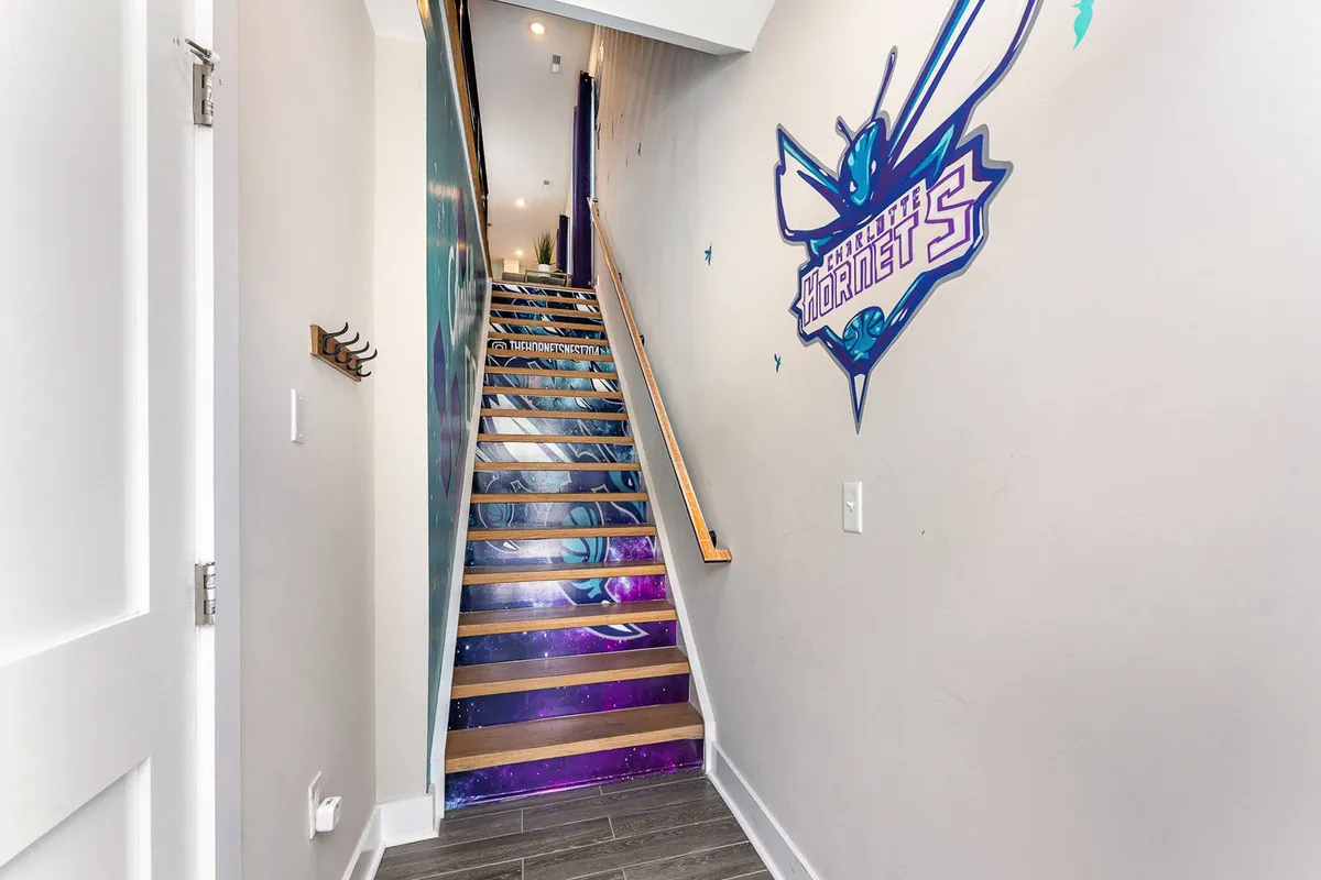 A staircase featuring a vibrant mural of the Charlotte Hornets logo and colorful wallpaper, creating an exciting transition area within the home. The design is youthful, energetic, and distinctly local, inspiring conversation and anticipation for what lies ahead upstairs.