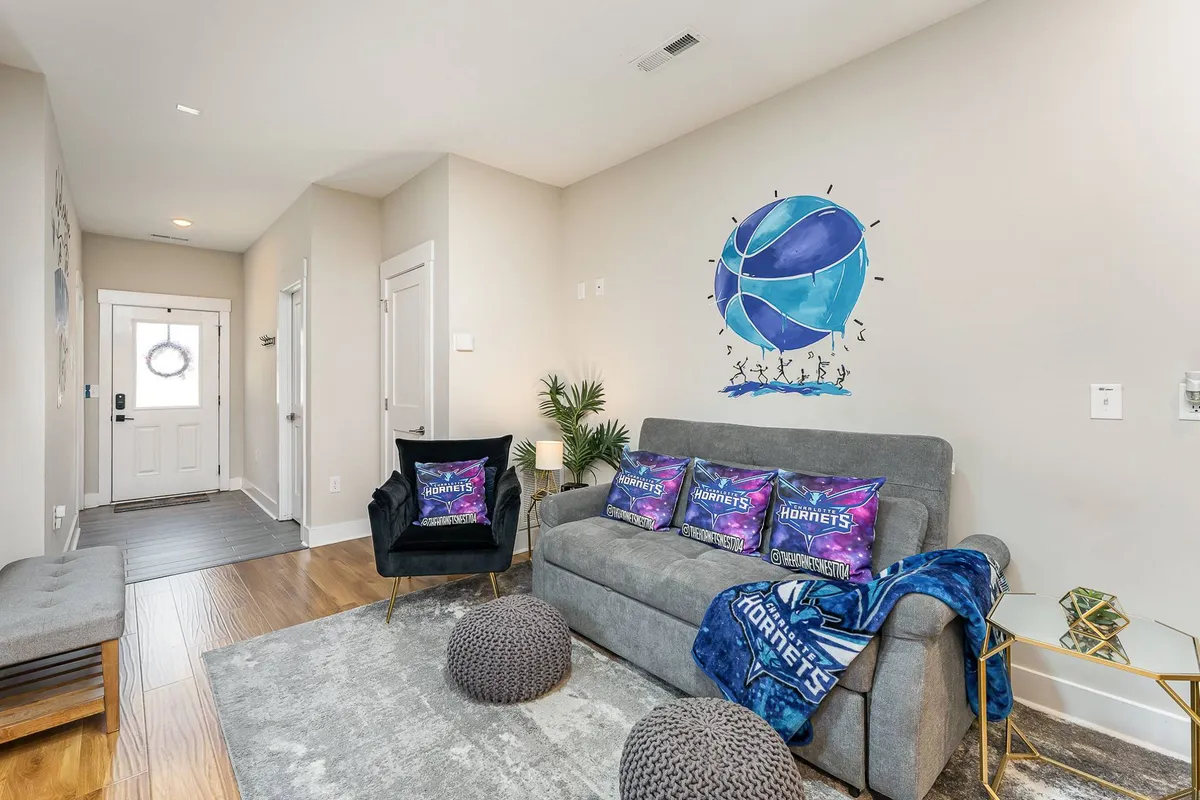 A playful and energetic living area with a basketball mural, colorful throw pillows, comfortable sofa, and accent chairs. The space is designed for entertaining friends, watching games, or hosting celebrations.