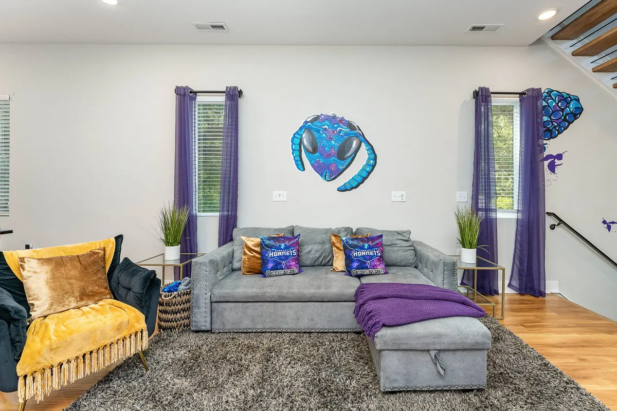 An inviting lounge space featuring bold, colorful wall art, a sofa with decorative pillows, a cozy armchair, and soft curtains. The setup exudes creative flair and offers a welcoming environment for guests to relax and connect.