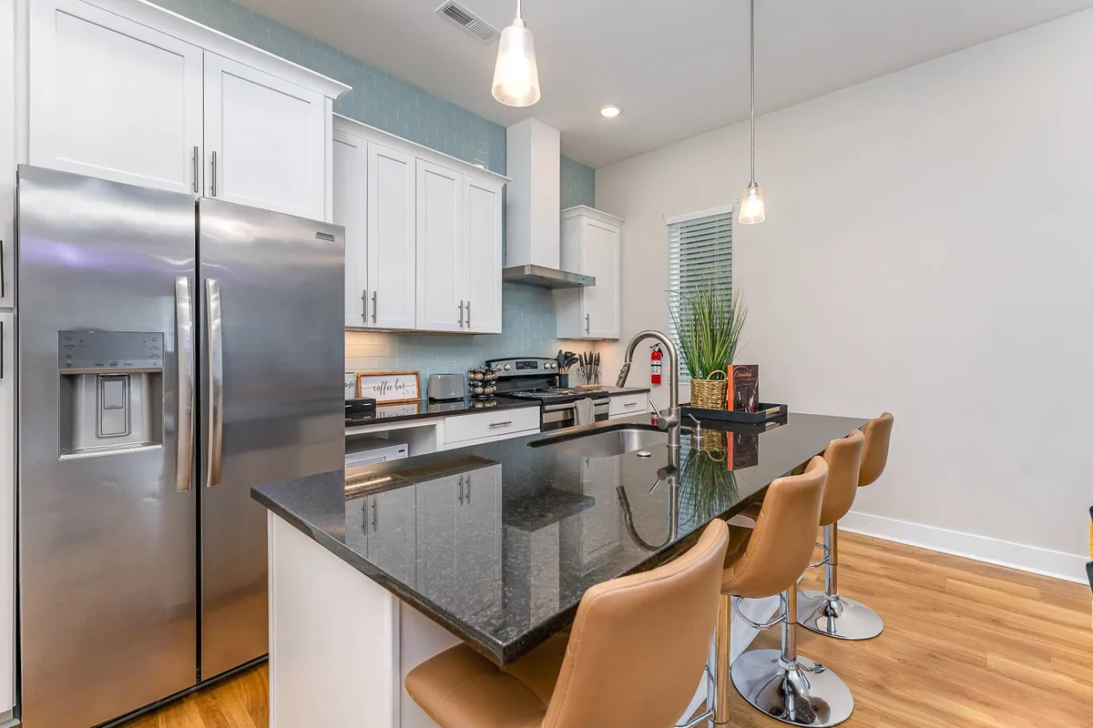 A modern kitchen with granite countertops, stainless steel appliances, bar stools, and decorative plants. The design emphasizes functionality and communal dining, supporting meal preparation for large groups or extended stays.