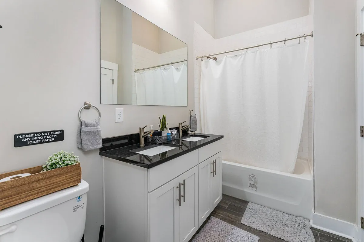 A serene bathroom with a double sink vanity, large mirror, and a bathtub with a shower curtain. The clean, organized environment speaks to the high standards of cleanliness and guest comfort.