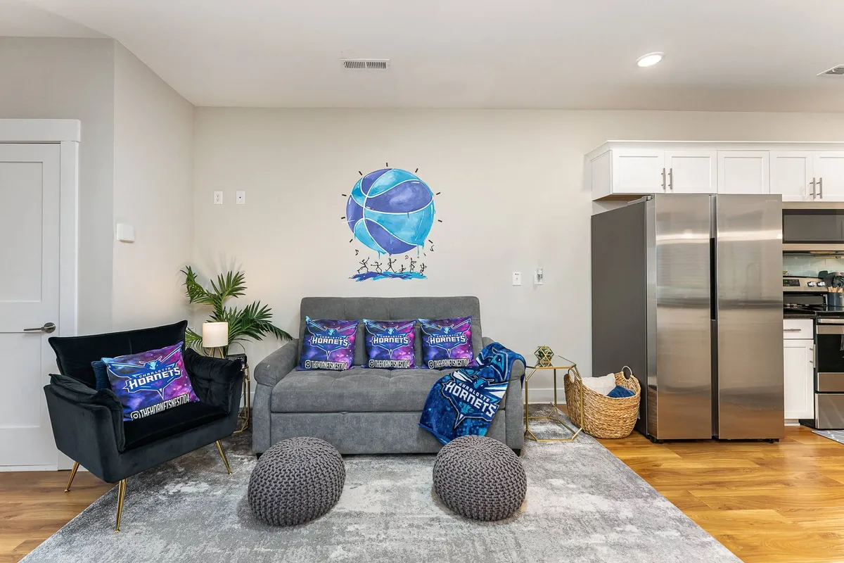 A stylish lounge area featuring a basketball-themed wall art above a comfortable sofa, accented with decorative pillows and unique poufs. The space is casual yet vibrant, inviting small groups to relax, socialize, or celebrate team wins after a productive day.